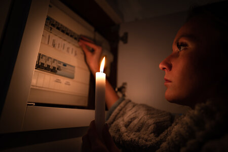 Een vrouw staat met een kaars bij de meterkast tijdens een stroomstoring